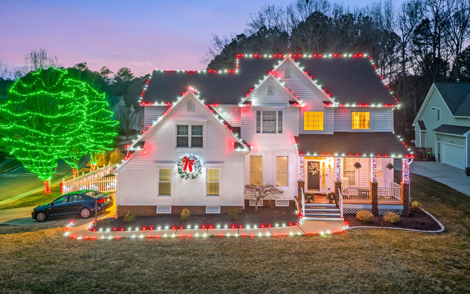 Holiday lighting installation by Monty's Lighting Co., serving Hanover County, VA — lit roofline with green-wrapped trees