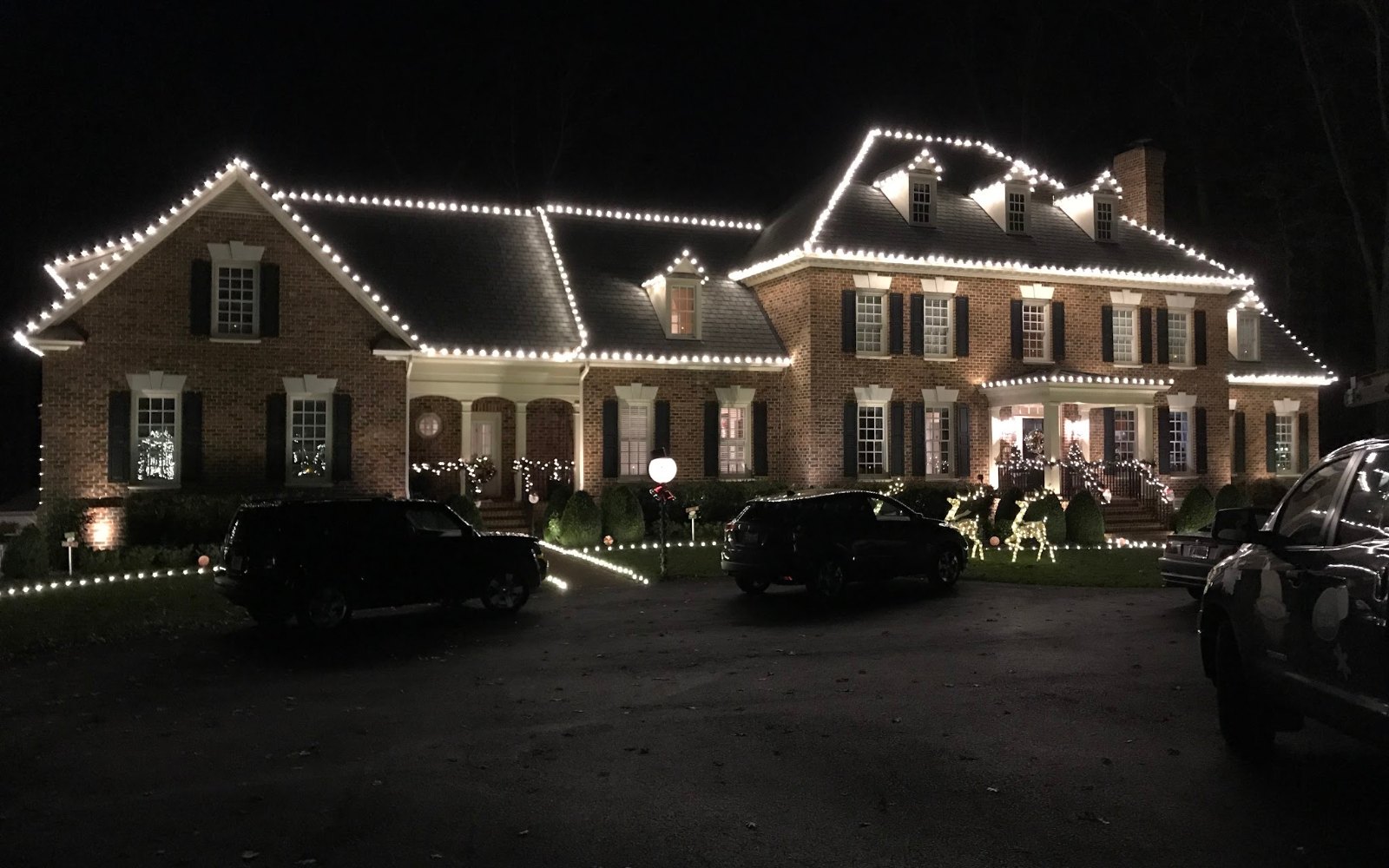 Christmas light installation by Monty's Lighting Co., serving Richmond, VA — warm white following the eaves and dormers of a brick colonial, wreaths in the windows
